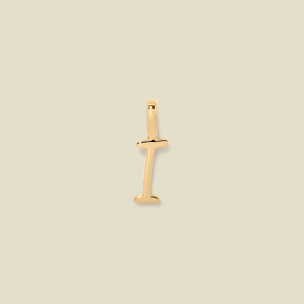 A polished gold initial pendant charm shaped like the letter 'I' in a cursive script, centered on a solid light beige background.