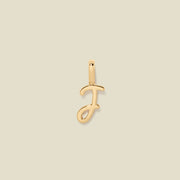 A polished gold initial pendant charm shaped like the letter 'J' in a cursive script, centered on a solid light beige background.