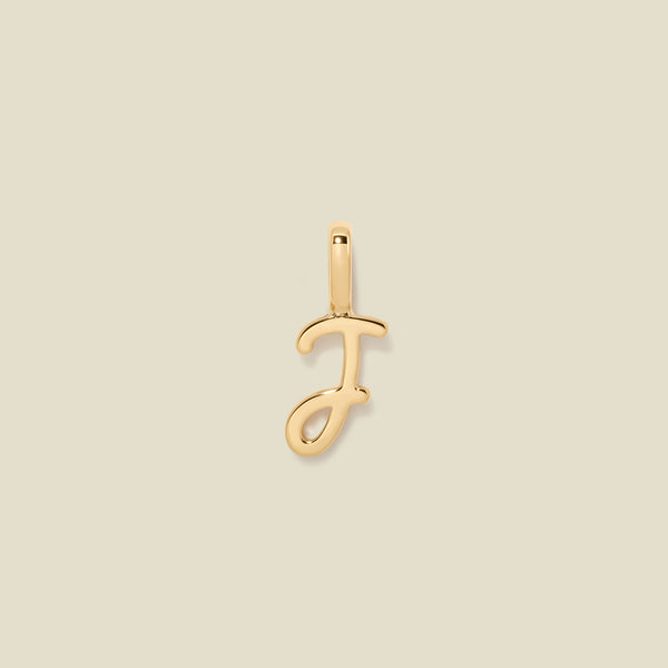A polished gold initial pendant charm shaped like the letter 'J' in a cursive script, centered on a solid light beige background.
