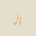 A polished gold initial pendant charm shaped like the letter 'N' in a cursive script, centered on a solid light beige background.