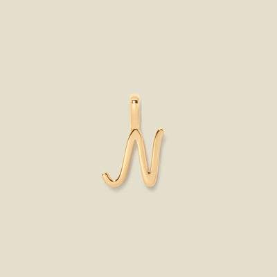 A polished gold initial pendant charm shaped like the letter 'N' in a cursive script, centered on a solid light beige background.