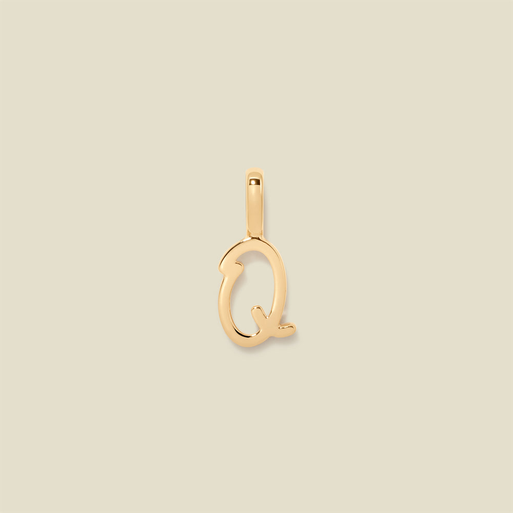 A polished gold initial pendant charm shaped like the letter 'Q' in a cursive script, centered on a solid light beige background.