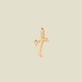 A polished gold initial pendant charm shaped like the letter 'T' in a cursive script, centered on a solid light beige background.