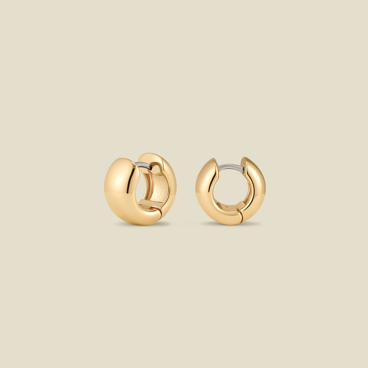 A pair of wide, polished gold huggie hoop earrings standing up right at two different angles, set against a solid beige background.