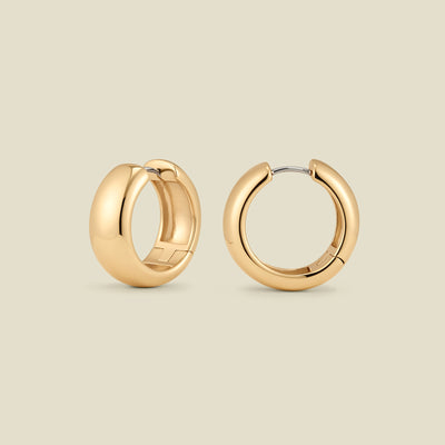 A pair of wide, polished gold hoop earrings standing up right at two different angles, set against a solid beige background.