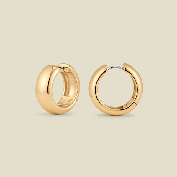 A pair of wide, polished gold hoop earrings standing up right at two different angles, set against a solid beige background.