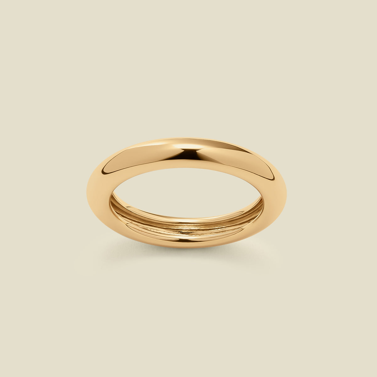 A polished, wide gold ring with a rounded domed exterior, set against a solid beige background.