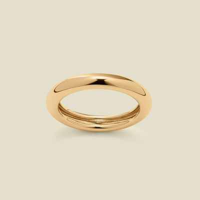 A polished, wide gold ring with a rounded domed exterior, set against a solid beige background.