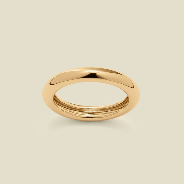 A polished, wide gold ring with a rounded domed exterior, set against a solid beige background.
