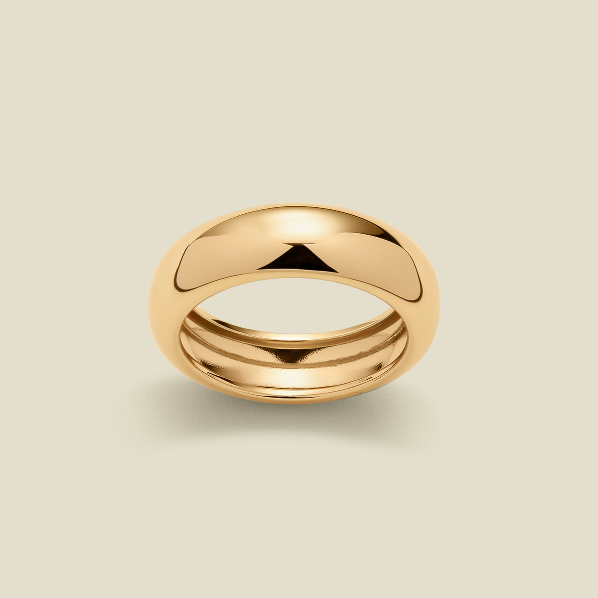 A polished gold band ring with a smooth, rounded dome-like top, shown on a light beige background.