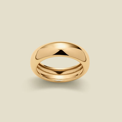 A polished gold band ring with a smooth, rounded dome-like top, shown on a light beige background.