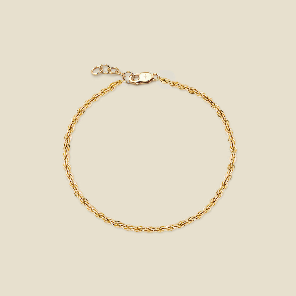 A gold rope chain bracelet with a lobster clasp and extender, displayed on a light beige background.