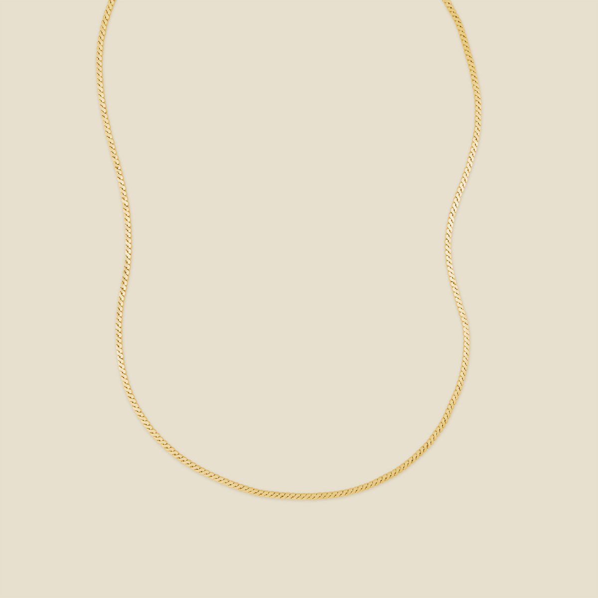 A gold flat, braided chain necklace set against a solid beige background.