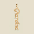 A polished gold script pendant spelling 'Grandma' vertically, shown on a solid light beige background.