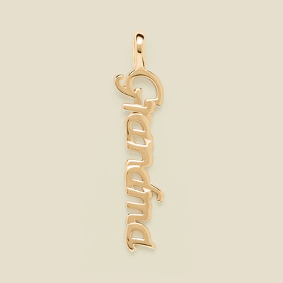 A polished gold script pendant spelling 'Grandma' vertically, shown on a solid light beige background.