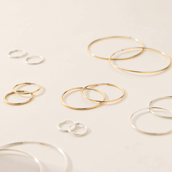 Three pairs of thin gold hoops and four pairs of thin silver hoops in varying sizes, laying flat against a solid white background.