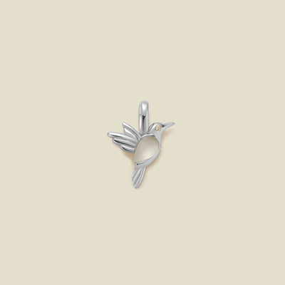 A silver hummingbird shaped charm featuring a translucent stone on the bodice, set against a solid beige background.