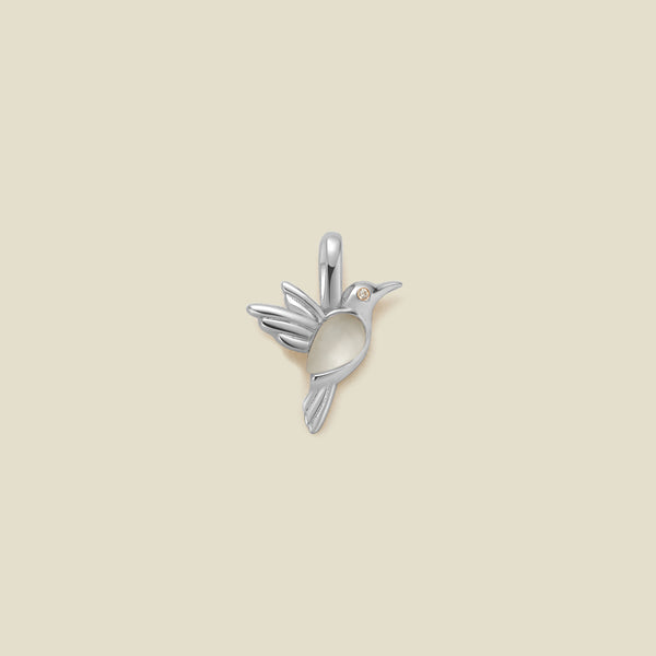 A silver hummingbird shaped charm featuring a translucent stone on the bodice, set against a solid beige background.