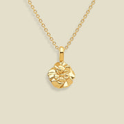 A gold necklace with a small, textured carnation flower pendant, displayed against a solid light beige background.