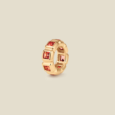 A gold ring charm with multiple bezel set square-cut red gemstones set side by side to create the band, shown on a solid beige background.