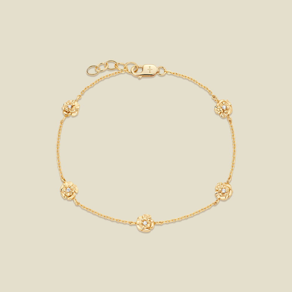 A delicate gold chain bracelet with five small, textured carnation charms spaced evenly along the chain, displayed on a solid light beige background.