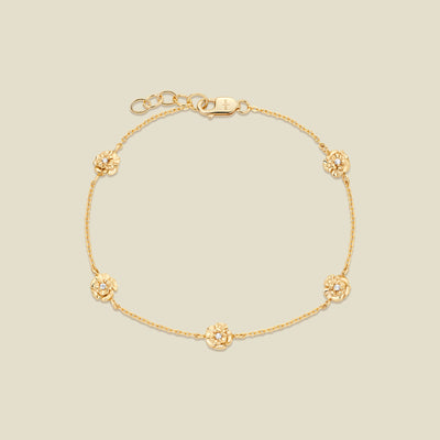 A delicate gold chain bracelet with five small, textured carnation charms spaced evenly along the chain, displayed on a solid light beige background.