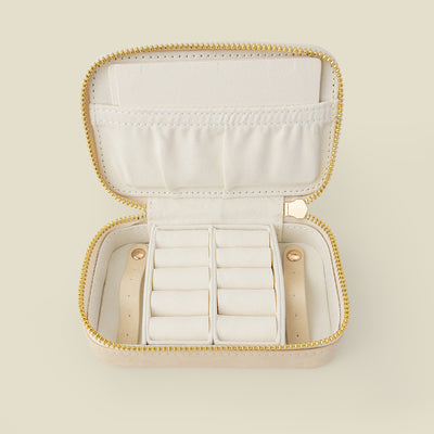 An open cream-colored jewelry organizer case with a gold zipper and white interior compartments, shown on a solid light beige background.