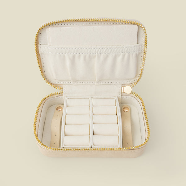 An open cream-colored jewelry organizer case with a gold zipper and white interior compartments, shown on a solid light beige background.