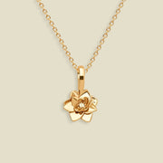A gold pendant necklace featuring a stylized lotus flower charm, suspended from a delicate gold chain against a solid light beige background.