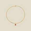 A delicate gold wire choker necklace with a small teardrop-shaped red gemstone pendant, displayed on a solid light beige background.
