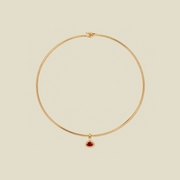 A delicate gold wire choker necklace with a small teardrop-shaped red gemstone pendant, displayed on a solid light beige background.