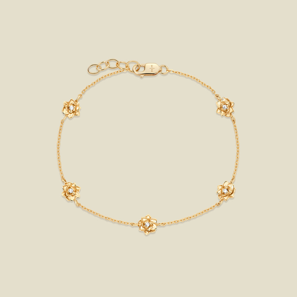 A delicate gold chain bracelet featuring five ornate, textured gold lotus charms with small clear stones, arranged in a circle on a light beige background.