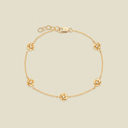 A delicate gold chain bracelet featuring five ornate, textured gold lotus charms with small clear stones, arranged in a circle on a light beige background.