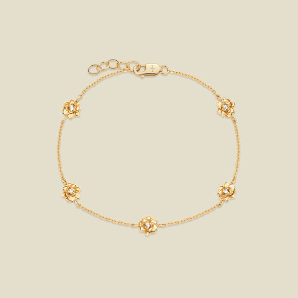 A delicate gold chain bracelet featuring five ornate, textured gold lotus charms with small clear stones, arranged in a circle on a light beige background.