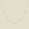 A delicate gold chain necklace featuring five small, evenly spaced textured lotus flower motifs set with tiny clear stones, displayed on a solid light beige background.