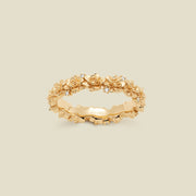 A gold floral-etched ring band with textured lotus flowers and small clear gemstones, shown on a plain warm beige background. 