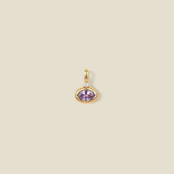 A gold oval pendant charm with a light purple bezel-set oval gemstone and a clear accent stone on top, set against a solid beige background.