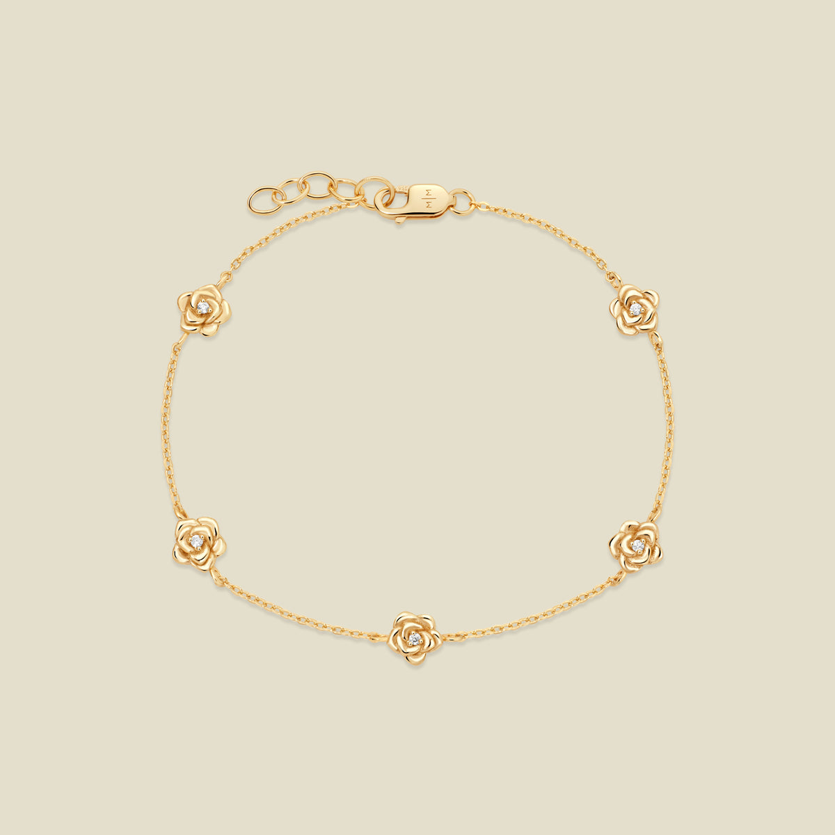 A delicate gold chain bracelet featuring five ornate, textured gold rose charms with small clear stones, arranged in a circle on a light beige background.