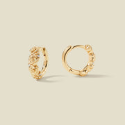 A pair of gold hoop earrings adorned with textured rose flowers stacked along the hoop, with scattered small clear accent stones, set against a solid beige background.