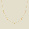 A delicate gold chain necklace featuring five small, evenly spaced textured rose flower motifs set with tiny clear stones, displayed on a solid light beige background.