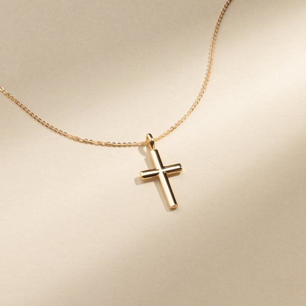 Gold cross pendant necklace on a beige background