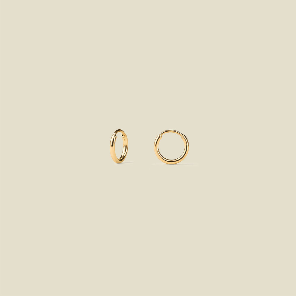 Two small gold hoop earrings shown on a plain warm beige background.