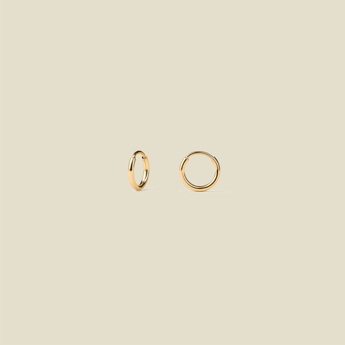 Two small gold hoop earrings shown on a plain warm beige background.