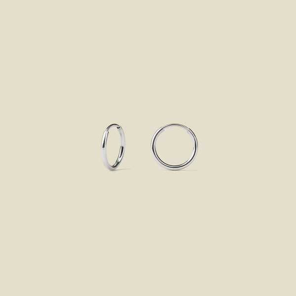 Two thin silver hoops, shown on a solid light beige background.