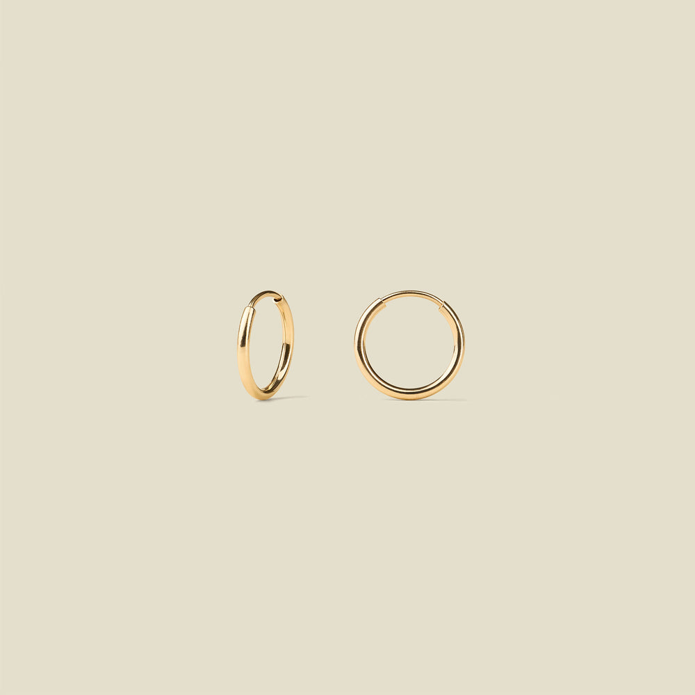Two minimalist gold hoop earrings shown on a solid light beige background.