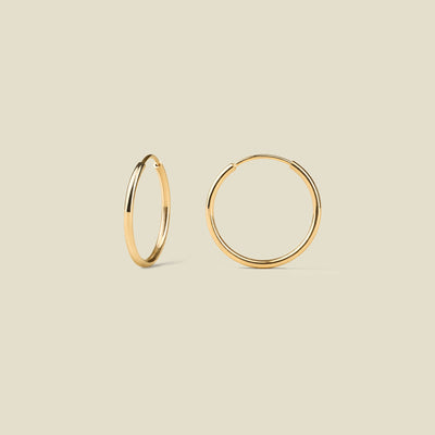 Thin gold hoop earrings on a beige background