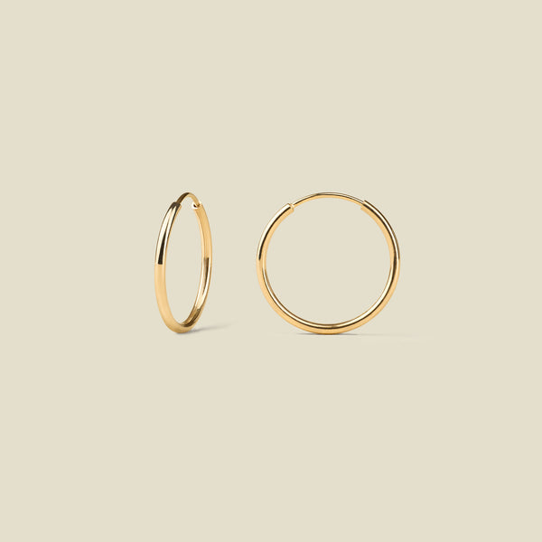 Thin gold hoop earrings on a beige background