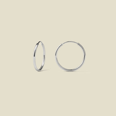 Pair of thin silver hoop earrings on a beige background