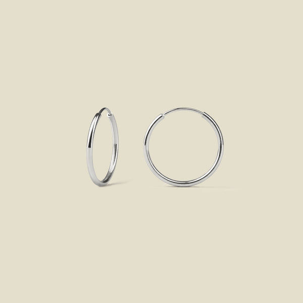 Pair of thin silver hoop earrings on a beige background