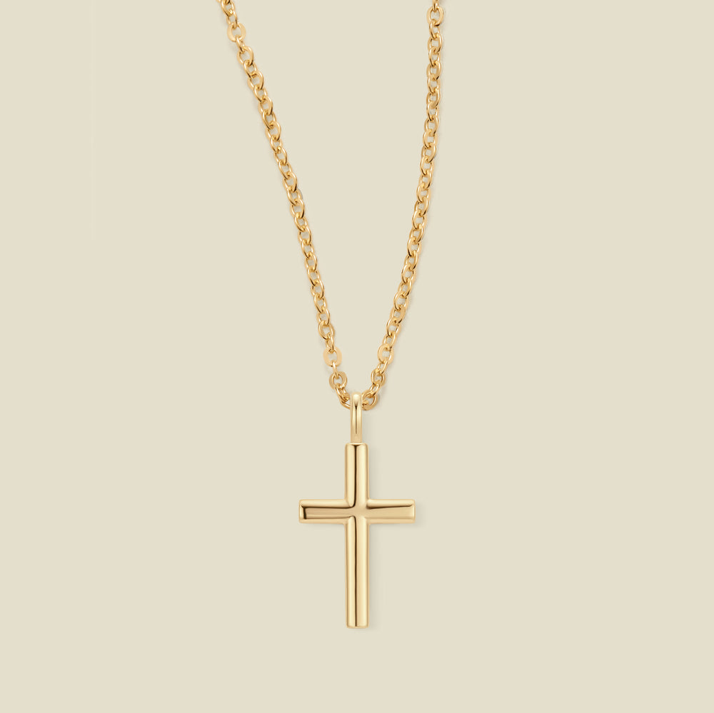 A gold cross pendant necklace on a delicate gold chain, centered against a solid light beige background.